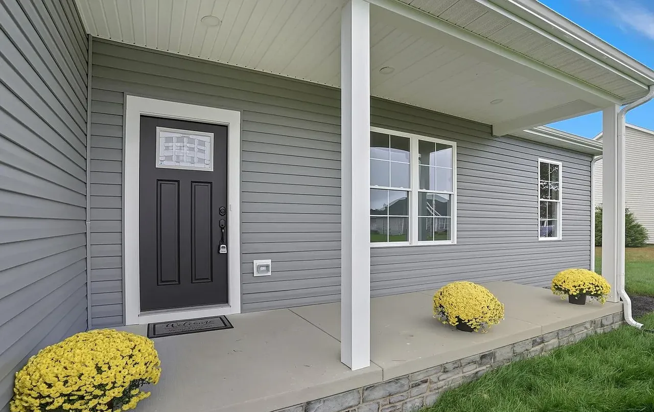 Covered front porch with dark panelled door, grey siding and autumn planting