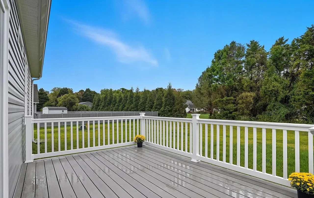 Rear deck with white railing overlooking an open lawn and treeline